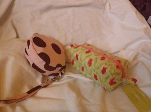 A circular zipped wristlet in pink and brown polka dots. Priced at $20. Shown with a large box bag made with a tulip fabric and a pink zip. It can hold everything! Priced at $14.